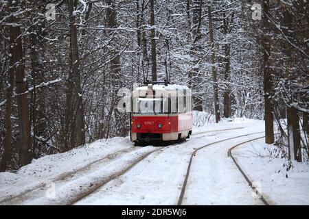 Kiev, Ukraine – 25 décembre 2018 : hiver enneigé. Le vieux tramway rétro rouge roule (va) le long de la route de banlieue. Arrière-plan d'hiver de la forêt de la ville Banque D'Images