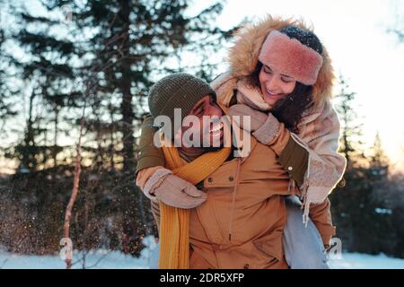 Riant un homme africain en vêtements d'hiver donnant son heureux fiançailles de petite amie tout en vous amusant et en profitant d'un week-end d'hiver dans un environnement naturel Banque D'Images