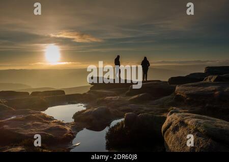 Deux personnes sur Stanage Edge regardant le soleil se coucher sur la vallée de l'espoir lors d'un après-midi hivernent en fin d'après-midi. Banque D'Images