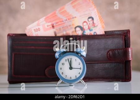 Réveil élégant pour cinq à douze personnes. En arrière-plan un portefeuille avec une pile d'argent bolivien collé. Cent billets de banque boliviano Banque D'Images