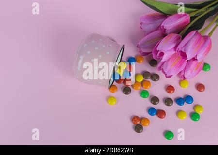 Une vie encore de bonbons colorés qui se répande d'un rose coupe à côté de tulipes roses sur fond rose Banque D'Images