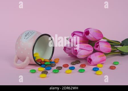 Une vie encore de bonbons colorés qui se répande d'un rose coupe à côté de tulipes roses sur fond rose Banque D'Images