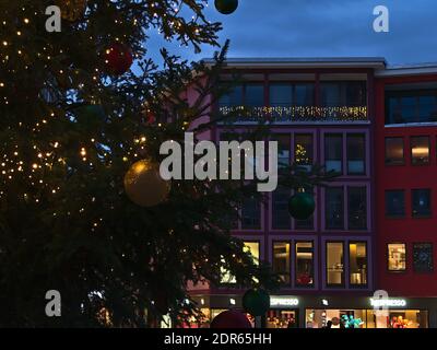 Arbre de Noël illuminé sur le marché avec des bâtiments commerciaux et des boutiques décorées en arrière-plan en soirée. Banque D'Images