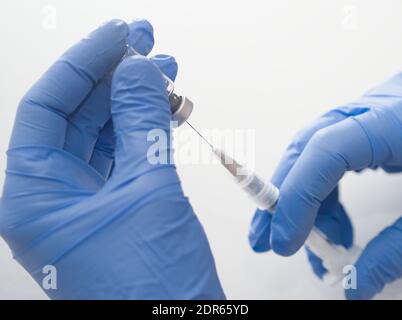 Mains dans des gants en caoutchouc bleu contenant une seringue et un flacon médicaux Gros plan sur fond blanc Banque D'Images