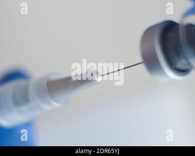 Mains dans des gants en caoutchouc bleu contenant une seringue et un flacon médicaux Macro gros plan sur fond blanc Banque D'Images
