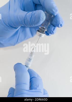 Mains dans des gants en caoutchouc bleu contenant une seringue et un flacon médicaux Gros plan sur fond blanc Banque D'Images