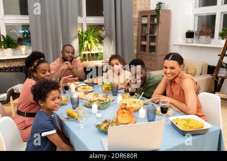 Grande famille africaine composée de père, mère, deux fils et filles réunis par table festive félicitant leurs amis dans le chat vidéo Banque D'Images