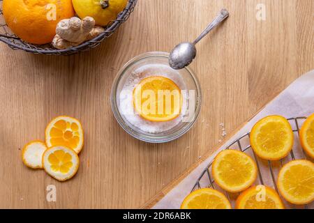 Faire des tranches d'orange confites: Table en bois avec des tranches d'orange séchées après cuisson au sirop, et un bol avec du sucre et une tranche d'orange. Banque D'Images