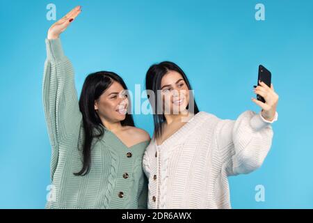 Les jumeaux brunette mignons dans les mêmes vêtements prennent un selfie sur un fond bleu. Passer du temps ensemble. Banque D'Images
