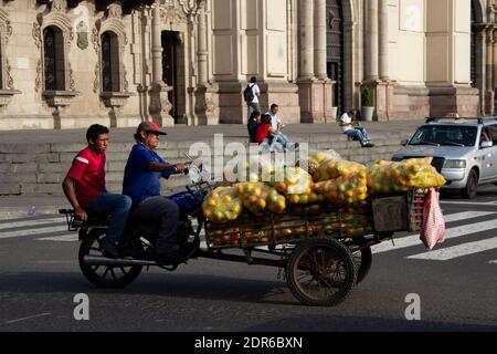 Lima, Pérou - 19 juin 2015 : deux hommes transportent un assortiment de fruits emballés dans des sacs en plastique qui seront vendus dans des stands de fruits dans les rues de la ville. Banque D'Images
