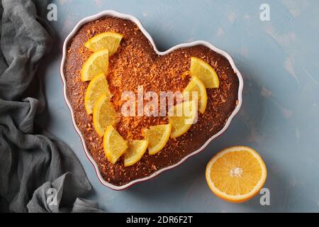 Gâteau fait maison aux oranges en forme de coeur parsemé de flocons de noix de coco colorés sur un fond bleu clair. Gros plan. Vue de dessus Banque D'Images