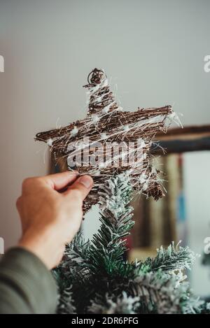 Une main masculine décorant l'arbre de Noël avec une étoile de topper, humeur de Noël Banque D'Images