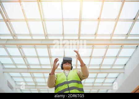Portrait graphique à faible angle d'une femme ingénieur portant un casque VR tout en visualisant un projet de conception architecturale sous un toit en verre, espace de copie Banque D'Images