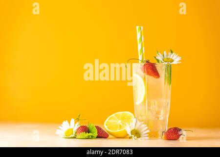 Verres de boisson fraîche glacée au citron et à la fraise. Arrière-plan jaune vif. Cocktails frais avec fruits de glace, herbes et camomille déc Banque D'Images