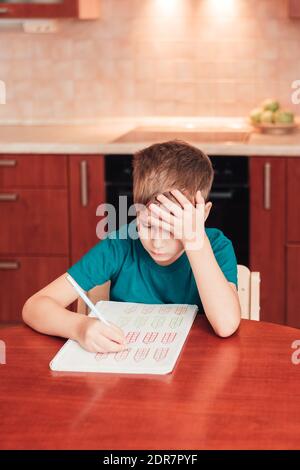 7 yeas vieux enfant assis à table dans la cuisine et faisant des exercices de mathématiques, devoirs difficiles, enfant se concentrant sur des exemples Banque D'Images