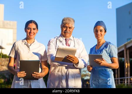 L'équipe latine de médecins regardent la caméra et Souriant en se tenant à l'extérieur de l'hôpital mexicain dans la ville de Mexico ou amérique latine Banque D'Images