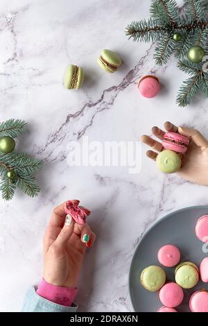 Macarons roses et vert menthe. Moitié mangé macaroni tenu dans la main femelle, et deux de plus en bois un. Dessert créatif vert et rouge sur une table en marbre Banque D'Images