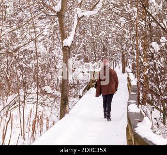 Un homme qui marche sur un pont en bois recouvert de neige en hiver à Frick Park situé à Pittsburgh, Pennsylvanie, États-Unis Banque D'Images