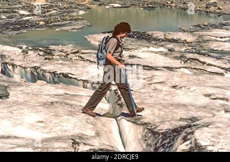 En utilisant une hache glacée pour la sécurité et le soutien, une femme de randonnée avec le service des parcs nationaux des États-Unis (NPS) traverse une fissure dans le reste glacial du glacier Grinnell, une attraction de longue date dans le parc national des Glaciers dans le nord-ouest du Montana, États-Unis. Le glacier a été nommé pour George Bird Grinnell, un ancien restaurationniste qui a découvert le champ de glace en 1885 et a aidé la région vierge à être établie comme le 10e parc national de l'Amérique en 1910. Malheureusement, les nombreux glaciers pour lesquels le parc est nommé ont souffert des changements climatiques au fil des ans. Banque D'Images