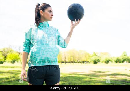 Jeune joueuse de football debout sur le terrain tenant le ballon. Banque D'Images