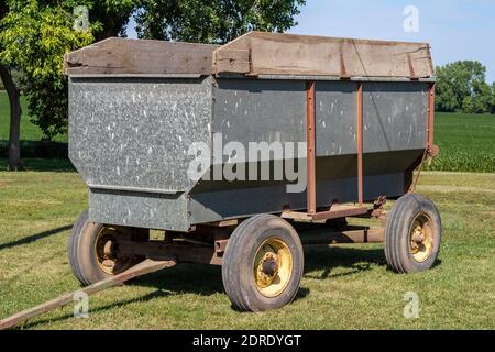 Gros plan sur un tracteur métallique d'époque équipé d'un outil agricole de wagon à grains tracté, avec un champ de récolte en arrière-plan Banque D'Images