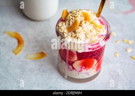 Flocons d'avoine d'une nuit avec banane, confiture de baies et noix de coco dans un pot en verre. Banque D'Images