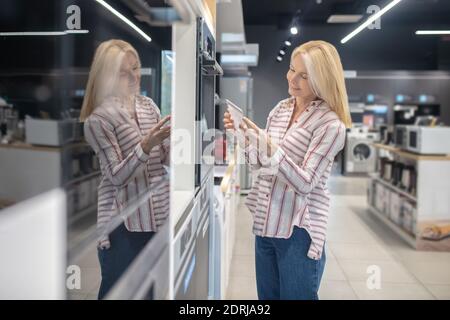 Client blond qui cherche à s'impliquer dans le choix d'un four dans une salle d'exposition Banque D'Images