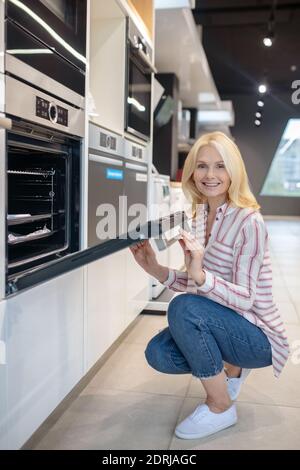 Client blond qui choisit un four dans une salle d'exposition et qui a l'air content Banque D'Images