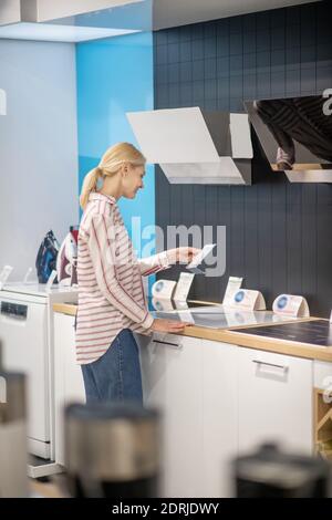 Une cliente blonde choisit des produits dans une salle d'exposition et regarde intéressé Banque D'Images