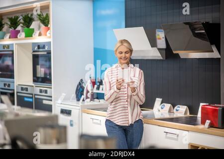 Une cliente blonde choisit des produits dans une salle d'exposition et regarde intéressé Banque D'Images