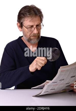 Un homme âgé attentionné lisant un journal avec une loupe isolé à la main sur fond blanc Banque D'Images