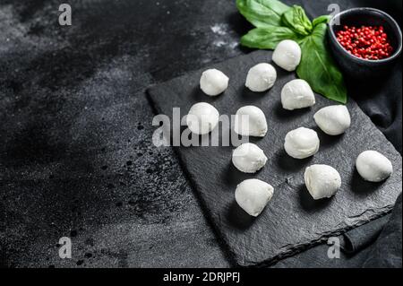 Mini boules de fromage mozzarella sur un plateau en pierre avec des feuilles de basilic et du poivre rose. Fond noir. Vue de dessus. Copier l'espace. Banque D'Images