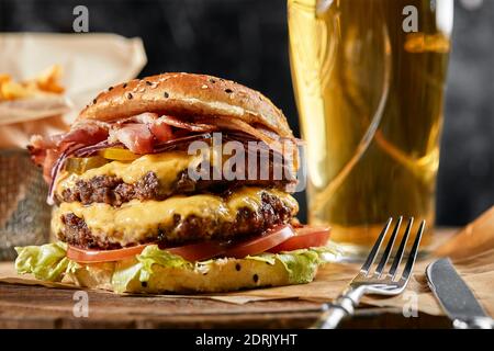 Le concept de restauration rapide américaine. Un hamburger américain juteux avec deux viandes de bœuf et une bière foncée sur fond de bois. Copier l'espace. Banque D'Images