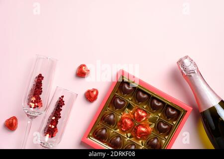 Bonne composition de la Saint Valentin. Plat, bouteille de champagne avec vue sur le dessus, verres, bonbons sur table rose. Amour, romance concept. Banque D'Images