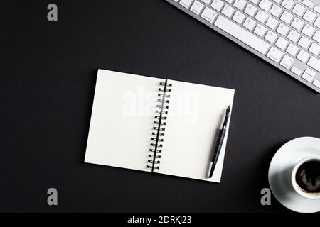 Table de bureau noire avec bloc-notes en papier vierge, stylo, clavier pc, tasse de café. Vue de dessus avec espace de copie, plan de travail. Espace de travail élégant. Business con Banque D'Images