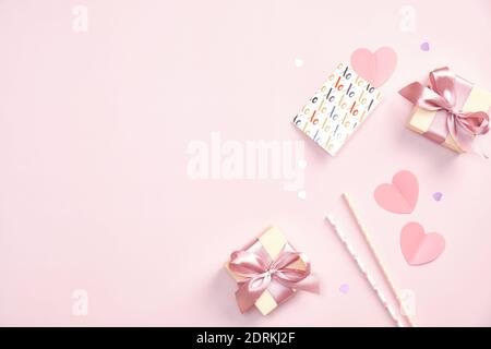 Concept de fête de la Saint-Valentin. Boîtes-cadeaux, carte de vœux, pailles à boire, coeurs en papier, confettis sur table rose. Flat lay, vue de dessus. Banque D'Images