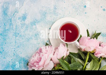 Tasse de thé et fleurs de péonies roses sur fond de pierre bleue. Vue de dessus avec espace de copie pour le texte. Cadeau pour femme ou fête des mères. Banque D'Images