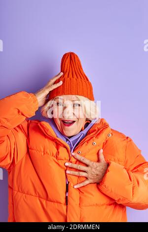 la femme mûre est surprise par quelque chose, tenez une main sur la poitrine, portant des vêtements d'hiver orange, isolés en studio Banque D'Images