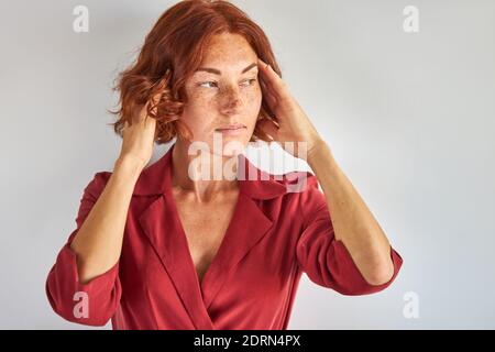 femme à tête rouge pensive en robe isolée, portrait en studio. femme avec des taches de rousseur et des cheveux rouges courts debout dans la contemplation Banque D'Images