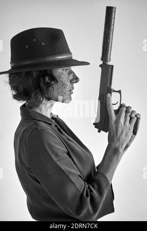 femme avec arme sur fond blanc, isolée. détective redhead femme dans le chapeau noir regardant loin, appliquant le canon de l'arme vers le haut Banque D'Images