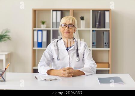 Médecin sérieux et mature écoutant le patient pendant un appel vidéo ou visite personnelle à la clinique Banque D'Images