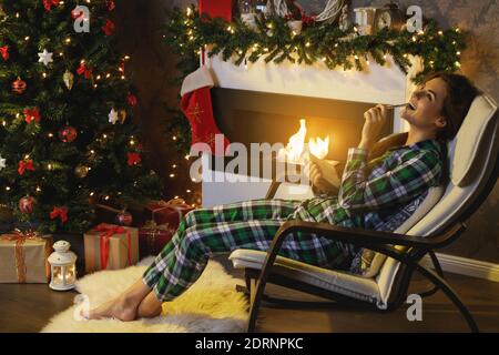 Bonne femme assise dans la chaise à bascule à côté de la cheminée et rédige le plan l'année suivante Banque D'Images