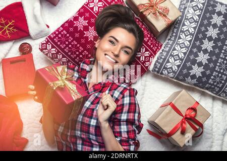 Une femme heureuse qui porte un pyjama à carreaux est couchée sur le sol Avec beaucoup de cadeaux de Noël Banque D'Images