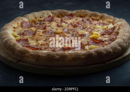 Délicieuse pizza au fromage, bacon croustillant et ananas sur fond sombre. Banque D'Images
