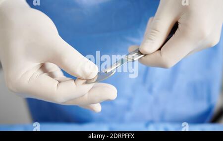 Vue rapprochée des mains du médecin se préparer au scalpel pour la chirurgie plastique. Chirurgien avec instrument médical en acier inoxydable dans les bras portant des gants stériles blancs. Concept de chirurgie et de médecine. Banque D'Images