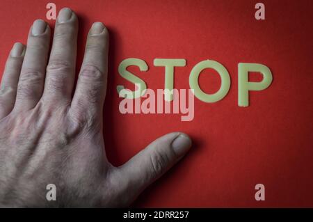 Main humaine à côté du mot Stop écrit avec des lettres en plastique sur fond de papier rouge, concept Banque D'Images