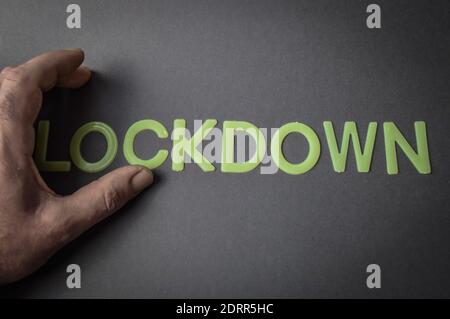 Doigts humains supprimant le mot Lockdown écrit avec des lettres en plastique sur fond de papier gris, concept Banque D'Images