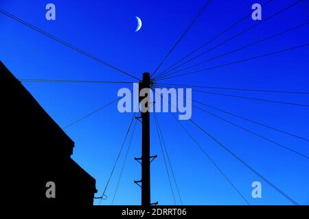 Communication de la perche de téléphone télégraphique et des fils de rayonnement le soir avec lune en croissant ciel bleu foncé Banque D'Images