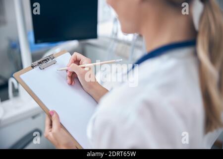 Une femme dentiste écrit sur une planchette à pince au bureau Banque D'Images