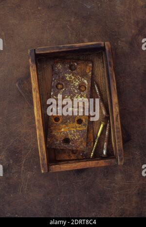 Petite ancienne boîte en bois contenant deux charnières de porte en métal rouillé et utilisé des vis en laiton et en métal Banque D'Images